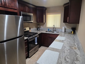 Una cocina con armarios de madera oscura, electrodomésticos de acero inoxidable, encimera de granito y una ventana con persianas.