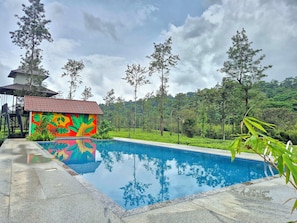 Una piscina con un mural colorido, rodeada de abundante vegetación y árboles.