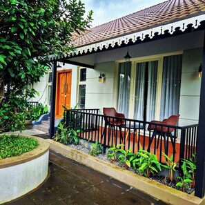 A covered outdoor area with a tiled roof, a wooden door, and a seating area with chairs.