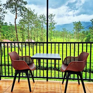 A terrace with two chairs and a table, overlooking a lush green landscape with trees and a distant mountain range.