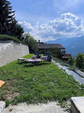 Eine Terrasse mit Liegestühlen, einer Steinmauer und Blick auf Berge.