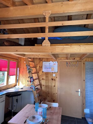 A wooden interior with a bunk bed, a kitchen area with a table set for dining, and a door with a coat rack.