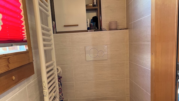 Een kleine badkamer met toilet, handdoekhouder, radiator en een weegschaal op de vloer.