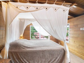 Une chambre avec un lit sous un dais, des murs en bois et une fenêtre donnant sur un paysage verdoyant.