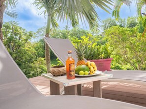 A table with a bottle, fruits, and a bowl on a deck with a view of greenery. - 3-star Villa Terrasses de Saint Protais with an unobstructed view of the country (Sainte-Anne)