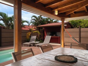 Une terrasse extérieure avec une piscine, des chaises longues et un espace barbecue couvert.