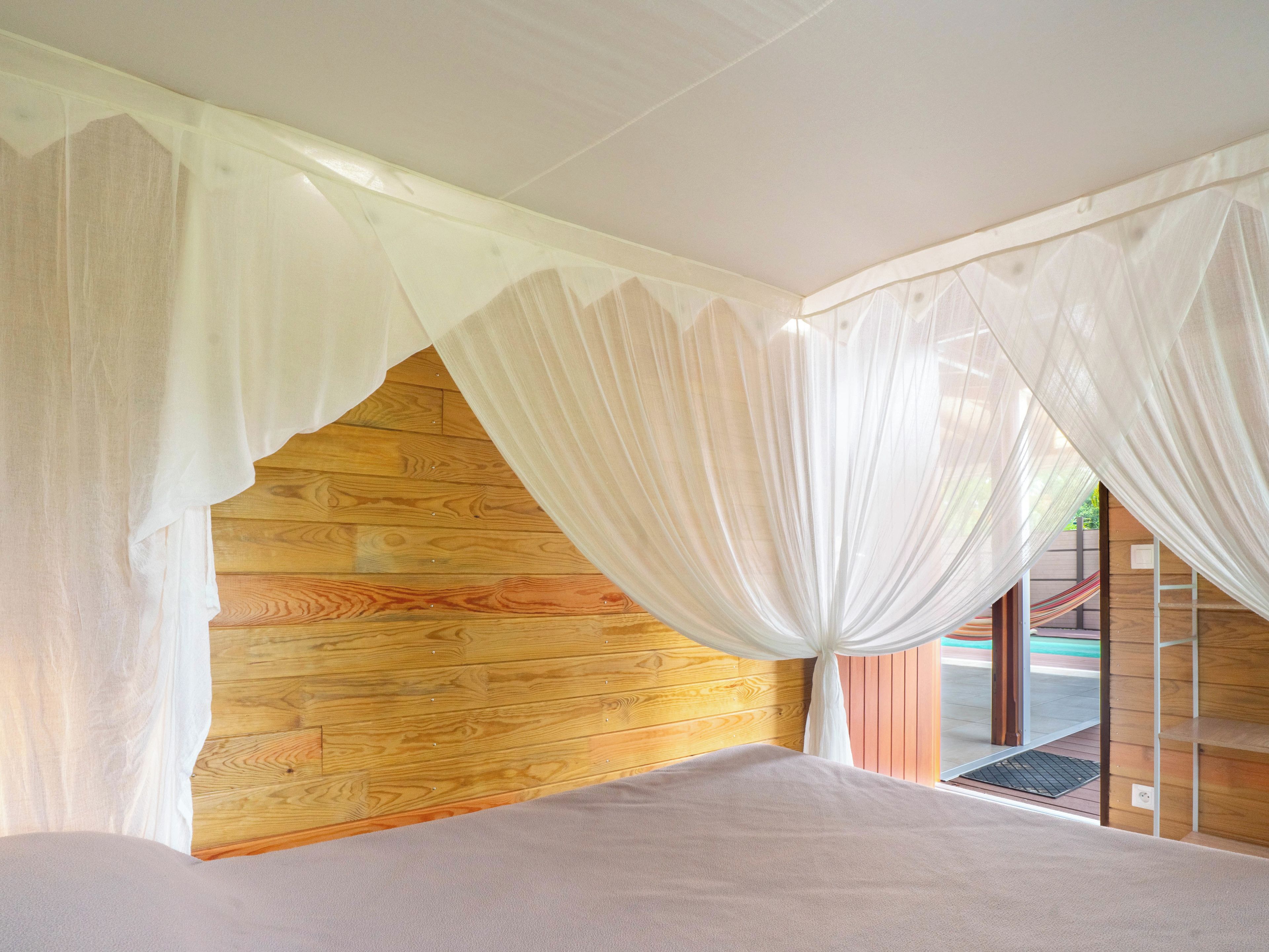 A bedroom with a wooden headboard, a bed with a white bedspread, and sheer white curtains.