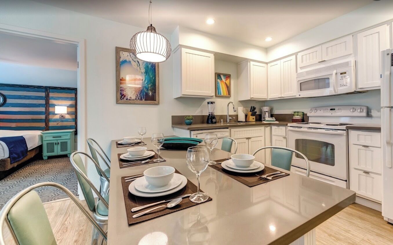 A modern kitchen with white cabinets, a central island with dining set, and a microwave above the stove.