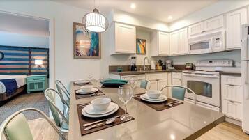 A modern kitchen with white cabinets, a central island with dining set, and a microwave above the stove.