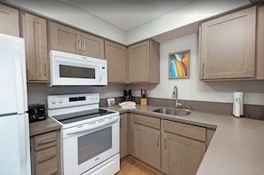Una cocina con armarios de madera, microondas, horno, fregadero y cafetera.