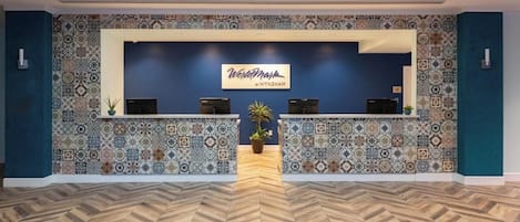 Un espace d’accueil avec un mur recouvert de carreaux décoratifs, un comptoir d’accueil et un parquet en bois disposé en chevrons.
