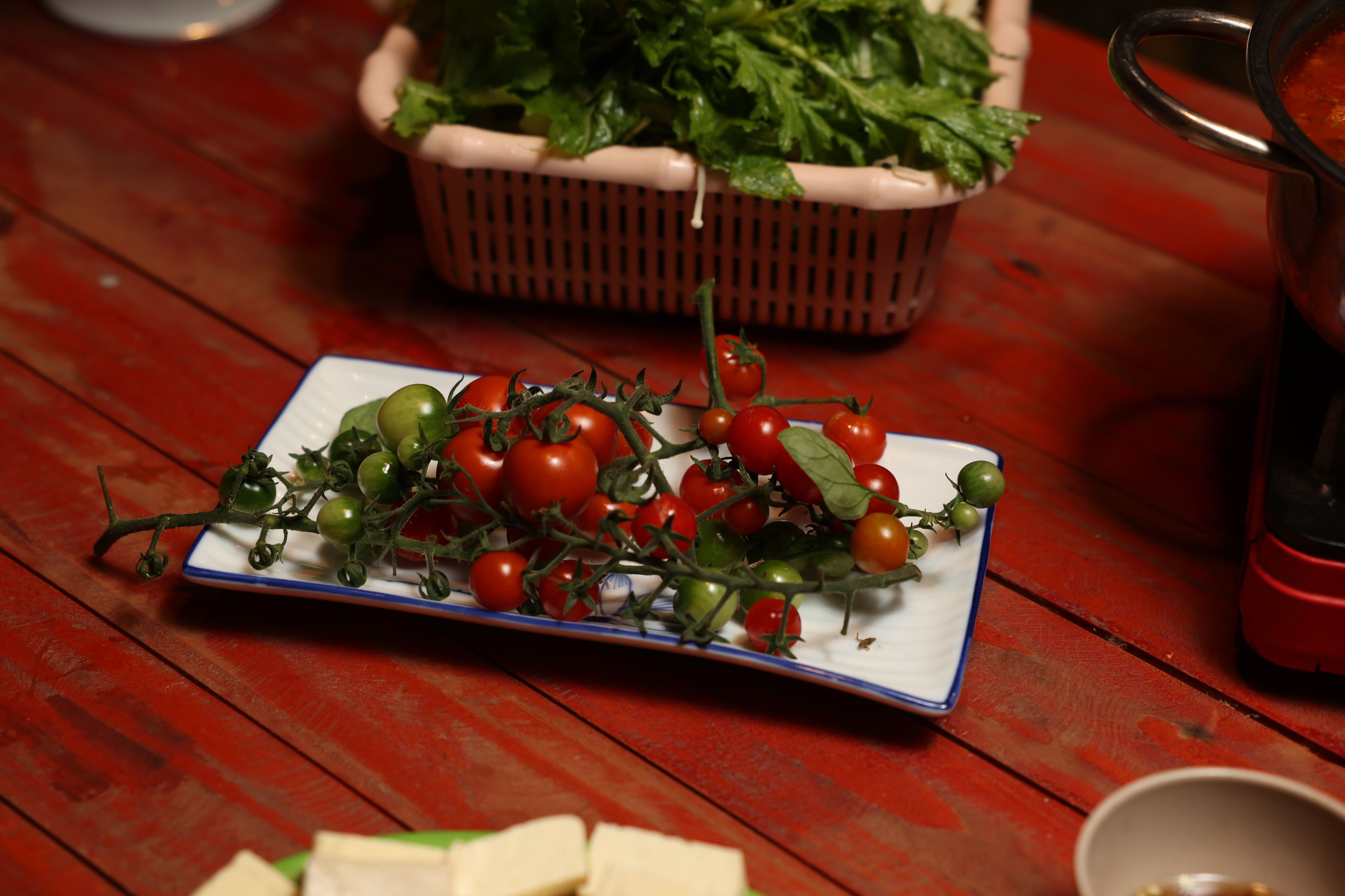 Un plato de tomates cherry variados y hojas verdes sobre una mesa de madera.