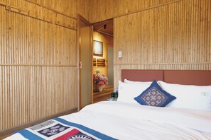 Habitación de hotel con pared de listones de madera, cama con ropa blanca y almohada estampada, y una mesita con un jarrón de flores.