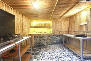 Interior de madera con paredes de piedra, piso de baldosas y una zona de cocina con ollas y sartenes.
