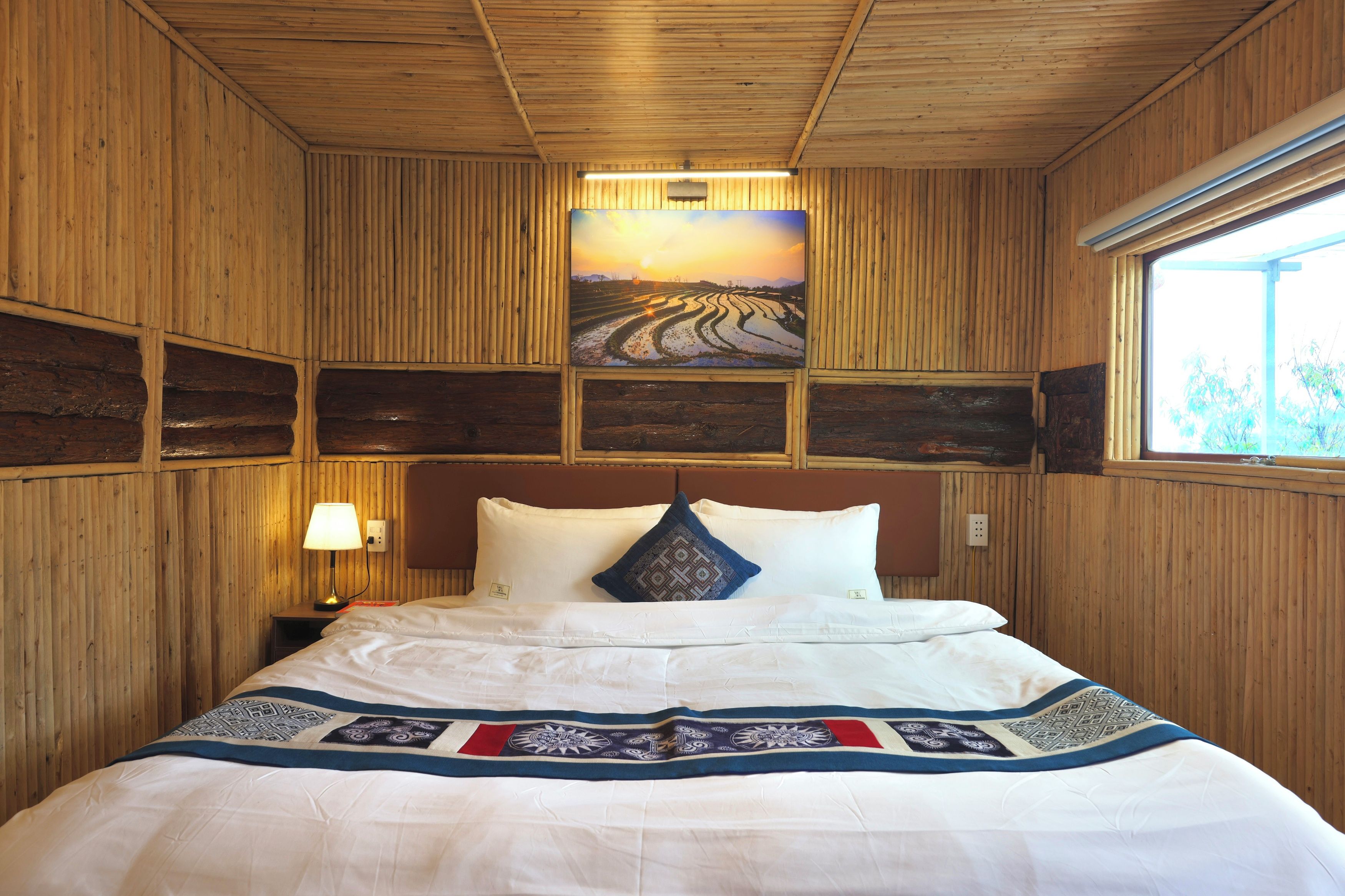 Una habitación con paneles de madera, una cama, una mesita de noche, una lámpara y un cuadro de un paisaje.