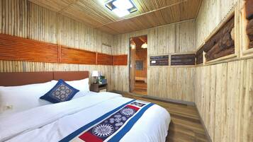 Un interior de madera con una cama, almohadas, una mesita de noche y una puerta que da a otra habitación.