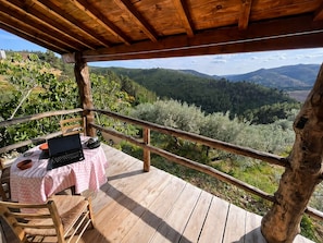 A wooden deck with a table and chair, overlooking a mountainous landscape.