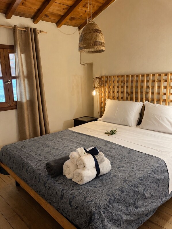 A bedroom with a bed, a nightstand, a hanging light fixture, and a window with curtains.