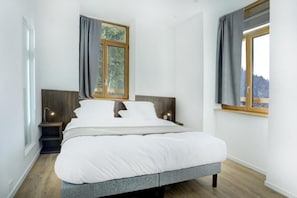 Quarto moderno com uma cama grande, duas mesas de cabeceira, janela com cortinas e vista para o exterior.