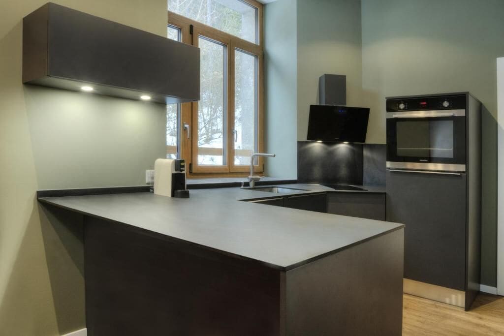 A modern kitchen with a central island, built-in oven, and a window with a view of trees.