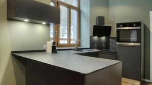 A modern kitchen with a central island, built-in oven, and a window with a view of trees. - Auberge de morcles (Lavey-Morcles)