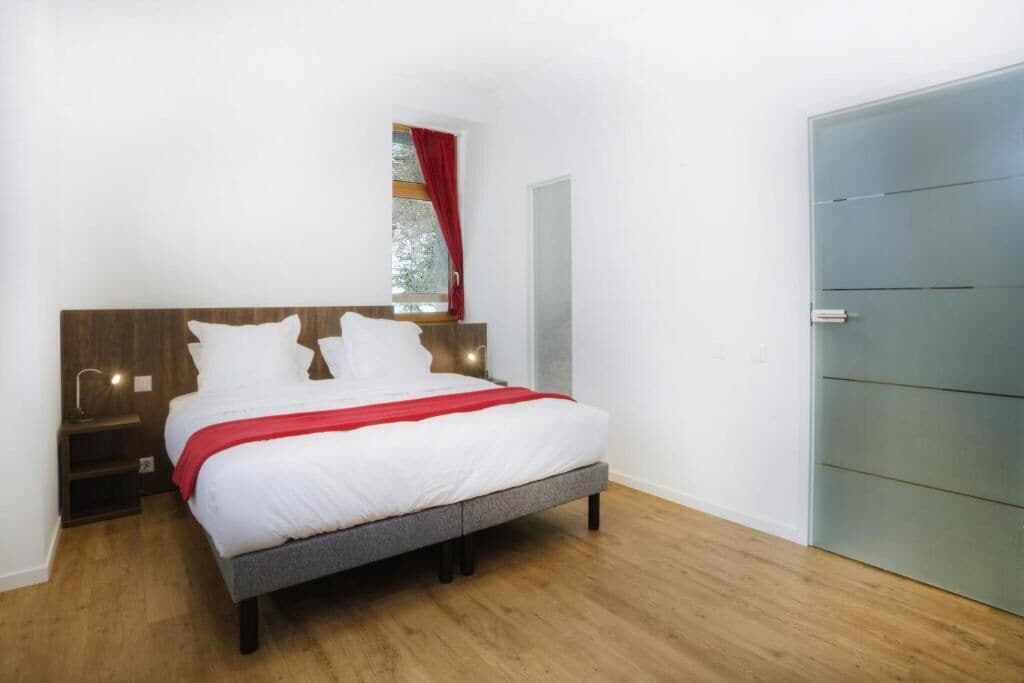 Une chambre à coucher avec un lit, une table de chevet, une fenêtre avec des rideaux et une porte.