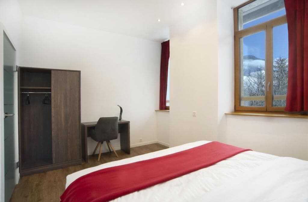 A bedroom with a bed, a desk, and a wardrobe.