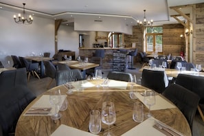 Restaurante com mesas redondas preparadas para refeições, área de bar e parede de pedra.