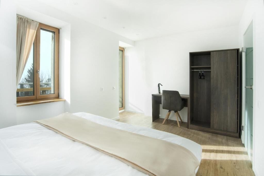 A modern bedroom with a large bed, a desk, and a wardrobe.