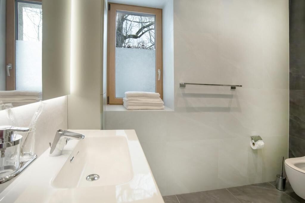 A modern bathroom with a white sink, a glass shower enclosure, and a window with a view of trees.