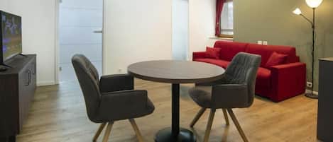 A modern living room with a round table and four chairs, a red sofa set, a television on a cabinet, and a floor lamp.