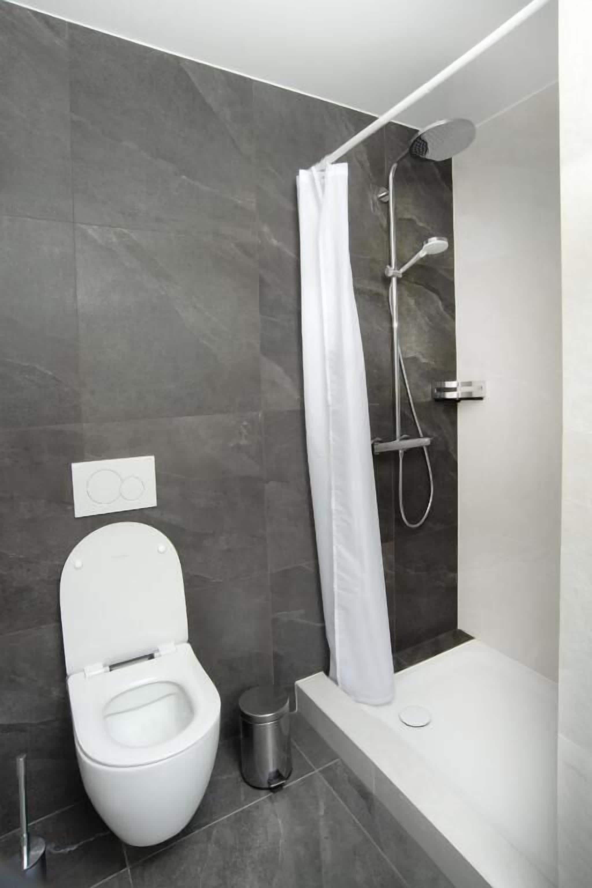 Un baño moderno con inodoro blanco, ducha con cortina blanca y bañera.