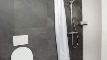 Un baño moderno con inodoro blanco, ducha con cortina blanca y bañera.