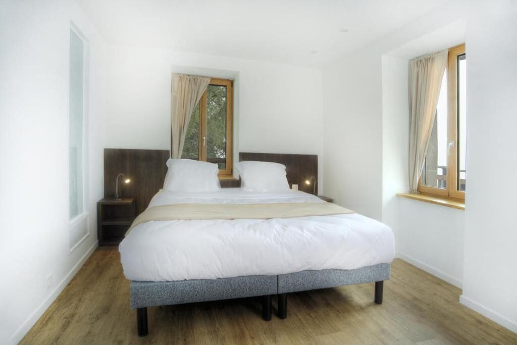 Un dormitorio con una cama grande, dos mesitas de noche, una ventana con cortinas y suelo de madera.