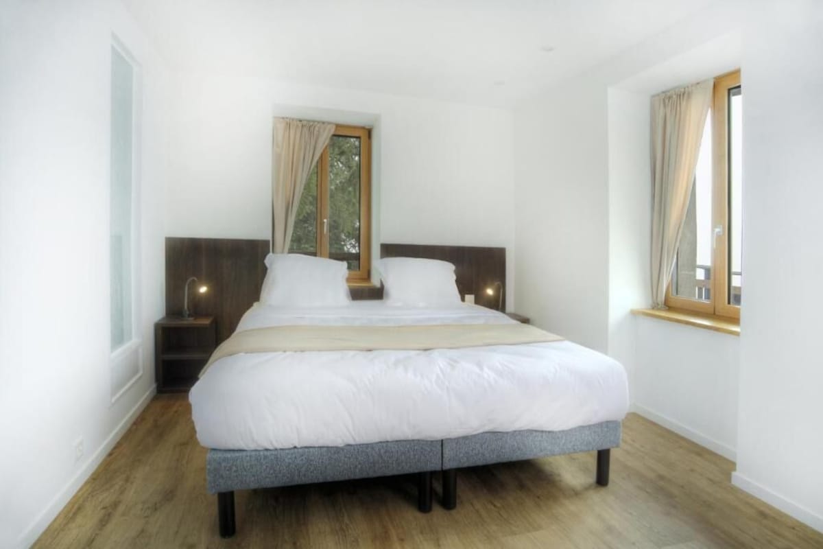 Quarto com cama grande, duas mesas de cabeceira, janela com cortinas e piso de madeira.