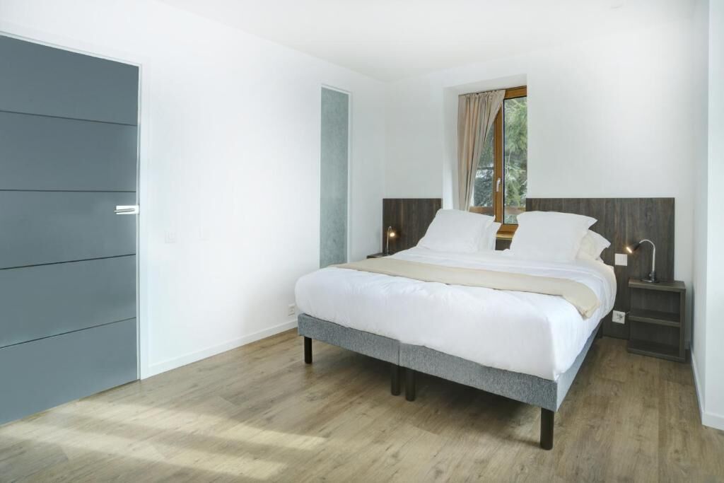 Un dormitorio con cama, mesitas de noche, armario y ventana con cortinas.
