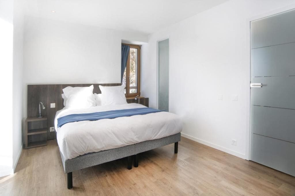 A bedroom with a bed, a nightstand, a window with curtains, and a door.