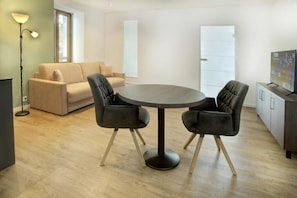 A modern living room with a round table, two chairs, a sofa, a floor lamp, and a television.