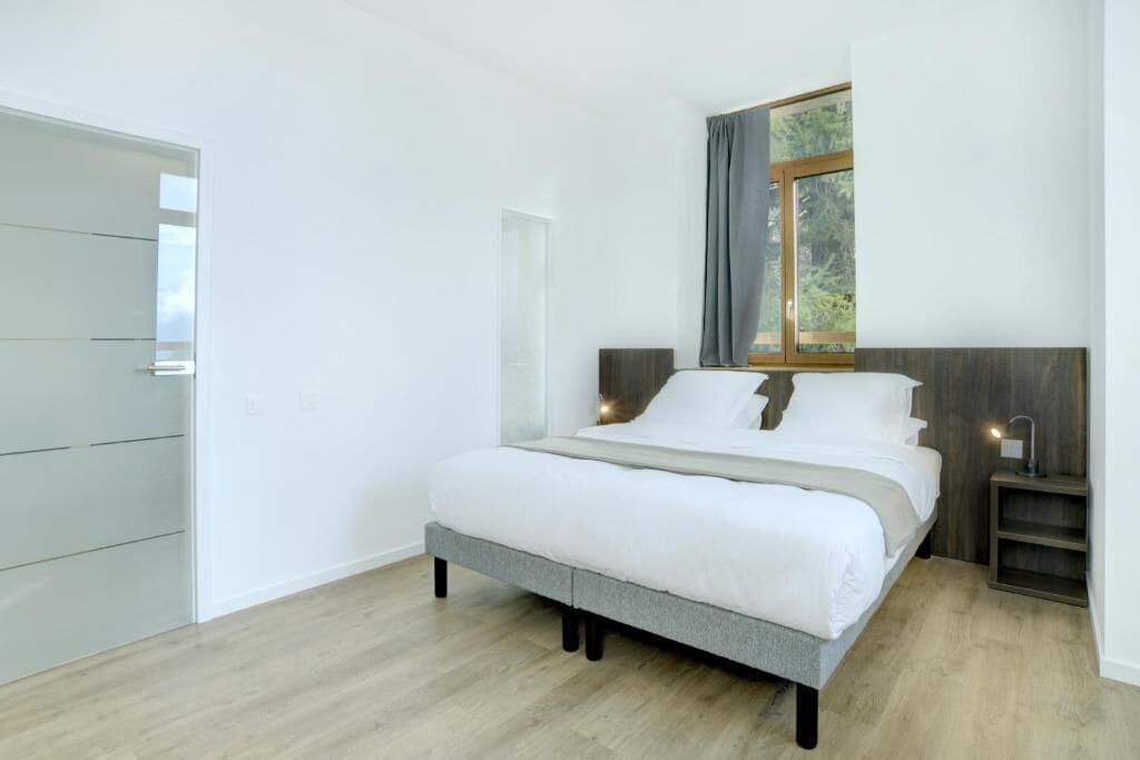 Un dormitorio moderno con cama, mesita de noche, ventana con cortinas y armario.