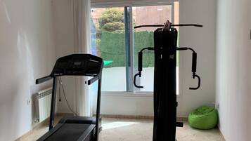Une pièce équipée d’un tapis de course, d’un appareil d’exercice multifonction et d’un fauteuil en forme de haricot vert.