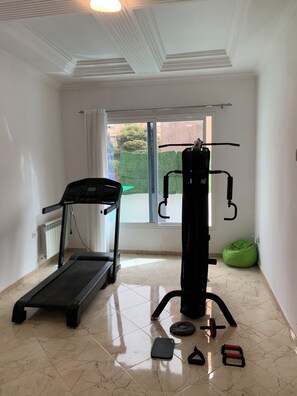 A room with a treadmill, a multi-functional exercise machine, and a green bean bag chair.