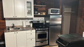 A compact kitchen with white cabinets, a stainless steel refrigerator, a microwave, a stove, and a sink.