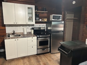A compact kitchen with white cabinets, a stainless steel refrigerator, a microwave, a stove, and a sink. - The Cedars Motel (Sicamous)