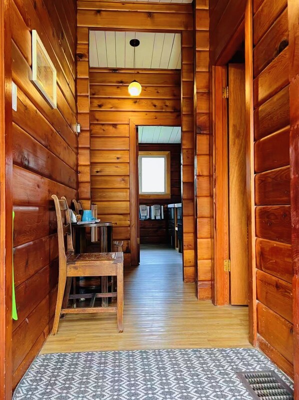 Un couloir intérieur aux murs en bois, avec une table et des chaises, une fenêtre et une porte donnant sur une autre pièce.