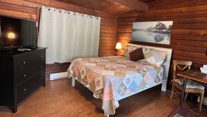 A wooden cabin bedroom with a bed, dresser, lamp, and a painting on the wall.