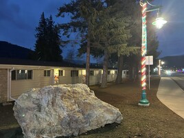 A row of cabins with a large rock in the foreground, a street lamp with colorful lights, and a mountain in the background.