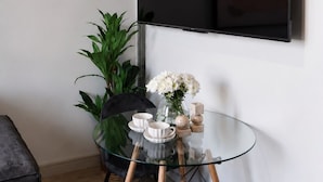 Een moderne kamer met een glazen tafel, een zwarte stoel, een potplant en een vaas met bloemen.