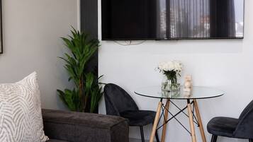 A modern living room with a grey sofa, a glass coffee table, and a black TV mounted on the wall.