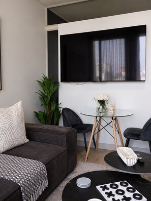 A modern living room with a grey sofa, a glass coffee table, and a black TV mounted on the wall.