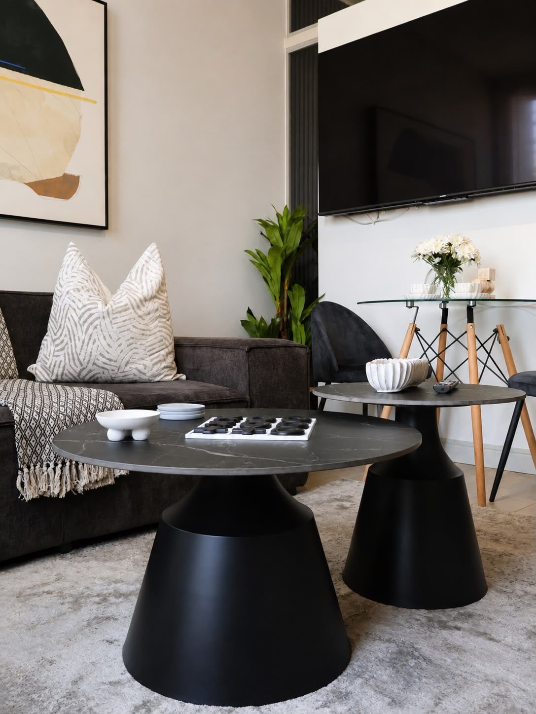 A modern living room with a sofa, two black coffee tables, a glass side table, and a flat-screen TV.